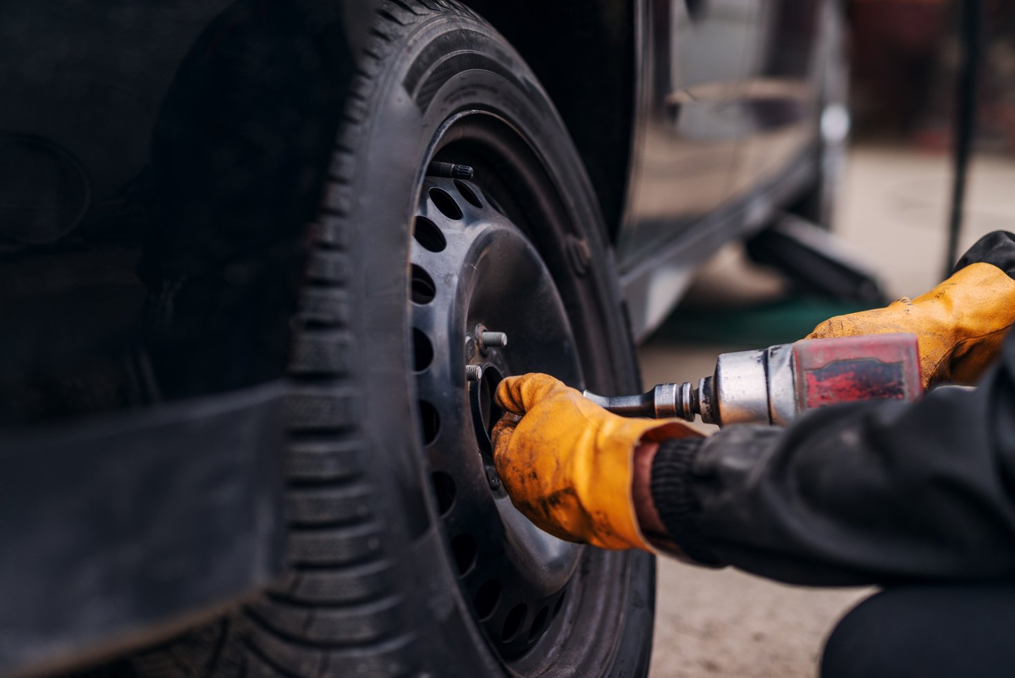 Auto mechanic with electric screwdriver changing tire outside. Car service. Tire installation.